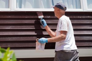 Man paints exterior cedar boards on house